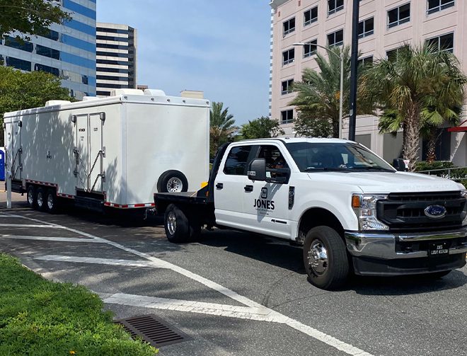 A Jones restroom trailer being pulled behind a white truck
